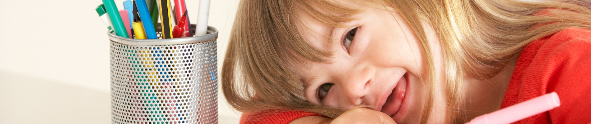 Enfant avec sourire joue avec des crayons.