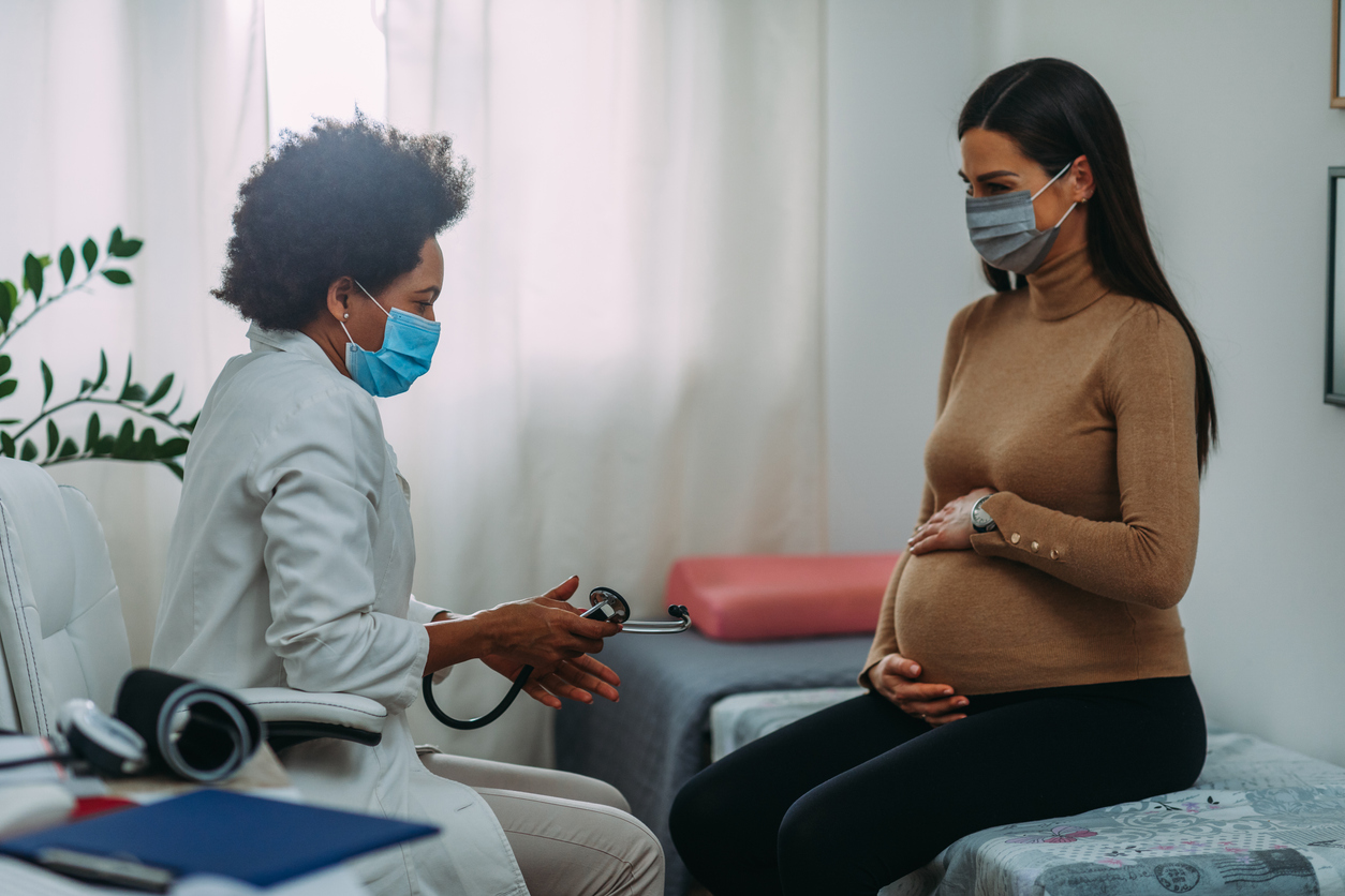 Une femme enceinte et sa médecin masque au visage, pendant un examen
