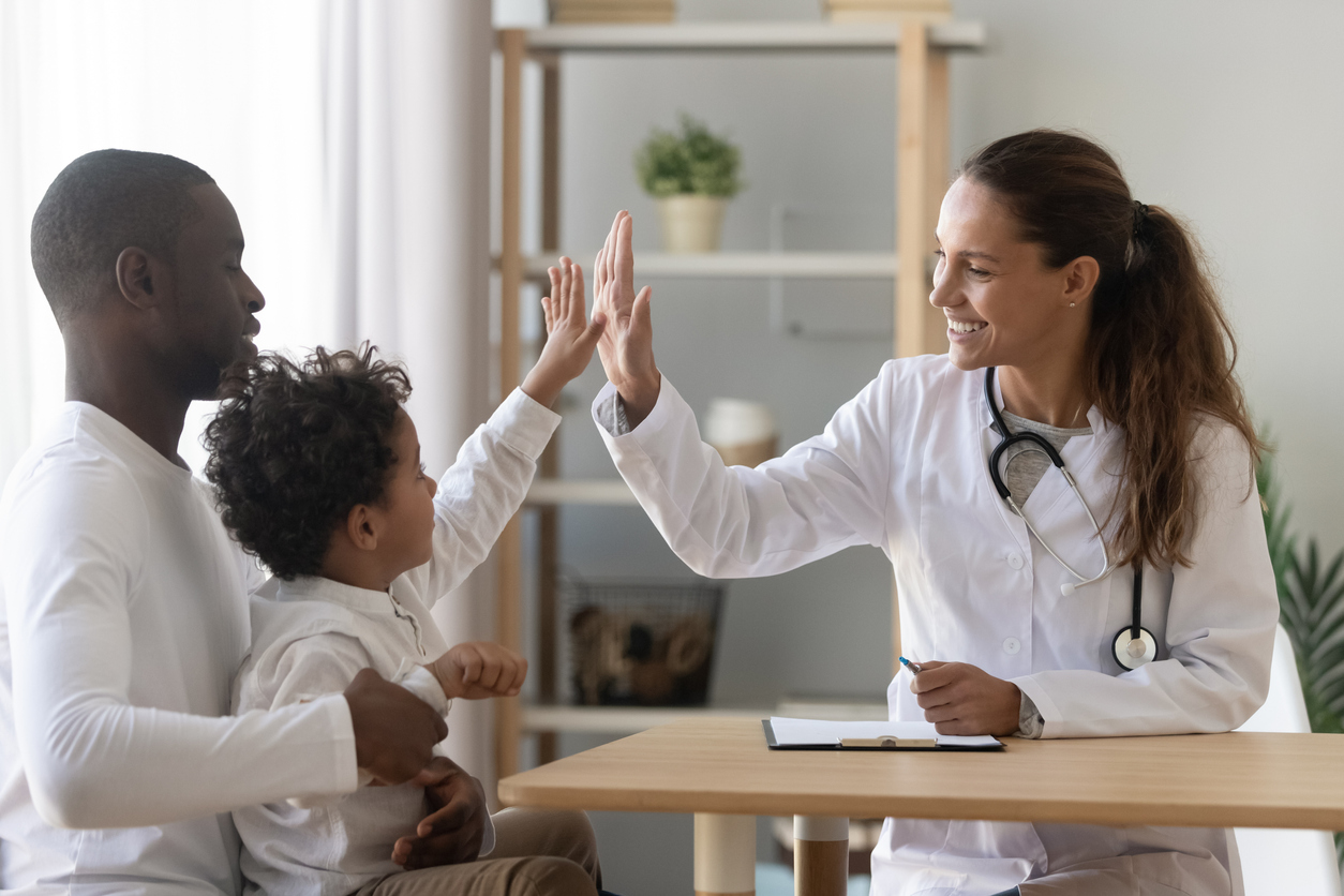 female physician giving high five to small boy on his Dad's lap