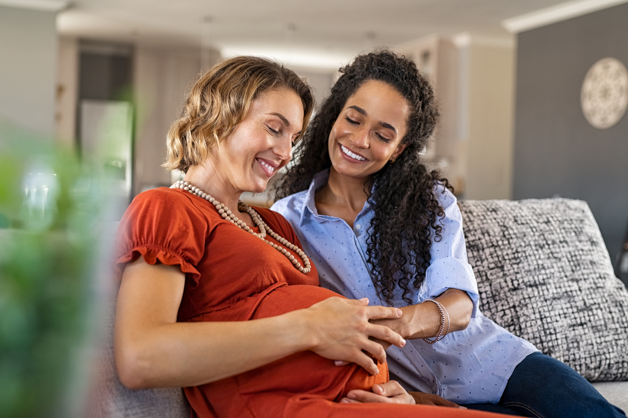 two women sitting on a couch, one is pregnant