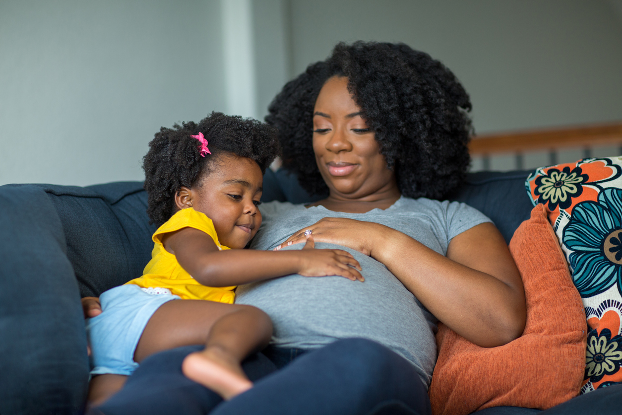 Femme enceinte sur un divan, la main d'une enfant sur son ventre 