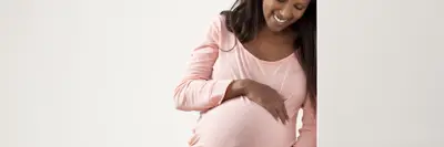A smiling pregnant person leaning against a wall holding her belly.